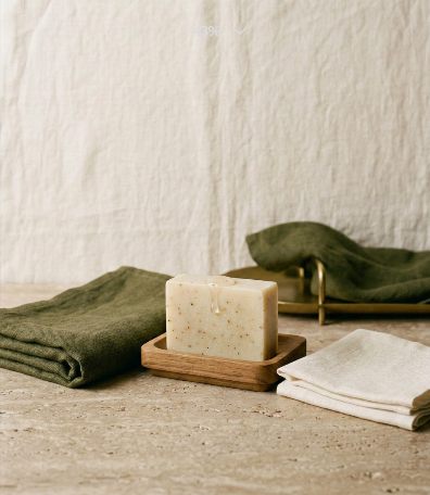 Bar of soap on a wooden dish beside folded linens